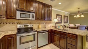 A kitchen with dark wooden cabinets, stainless steel appliances, a granite countertop, and recessed ceiling lighting.
