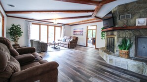 A spacious living room with a stone fireplace, wooden beams, and large windows. - An Updated, Secluded family friendly home with Fast Wifi (Manhattan)