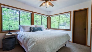 A bedroom with a large bed, multiple windows, a ceiling fan, and a nightstand. - An Updated, Secluded family friendly home with Fast Wifi (Manhattan)