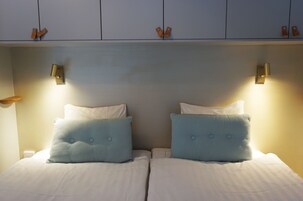 Una cama doble con dos almohadas, una mesita de noche y un estante en la pared con dos etiquetas anaranjadas.