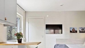A modern bedroom with a bed, a desk, and a chair. There is a window with a view of trees and a door. - Avanti Hotel (Hägersten)