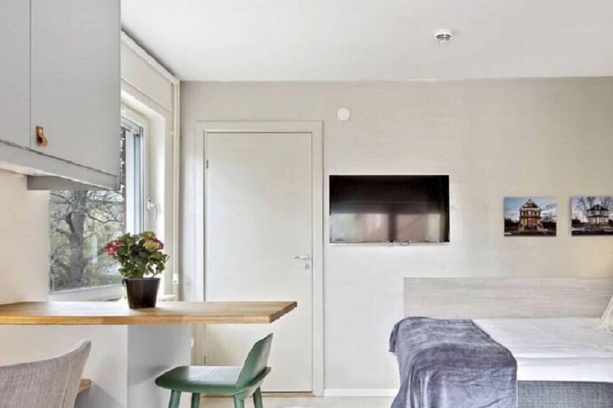 A modern bedroom with a bed, a desk, and a chair. There is a window with a view of trees and a door.