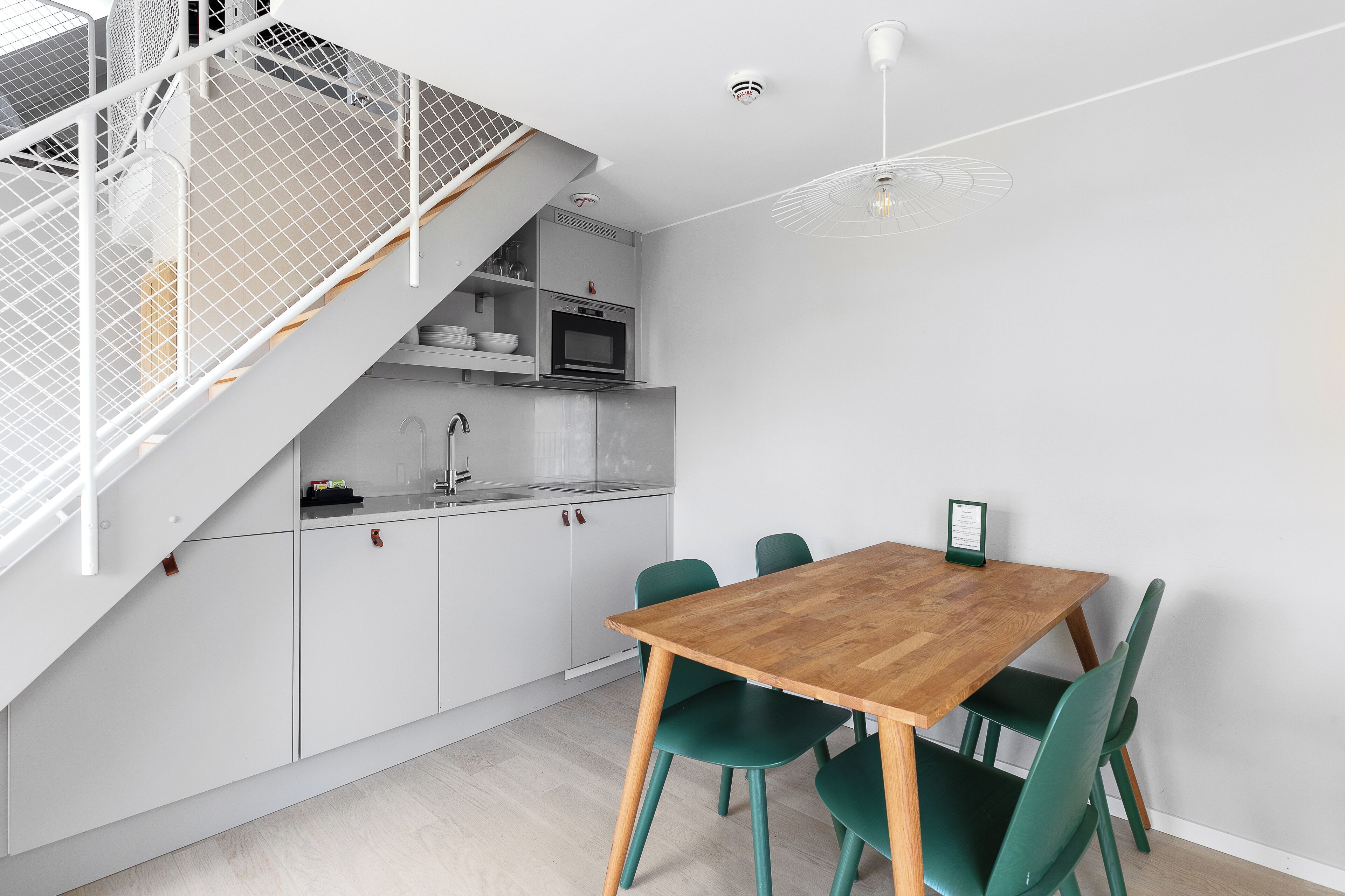 Una cocina moderna con armarios blancos, una mesa de comedor de madera y sillas verdes.