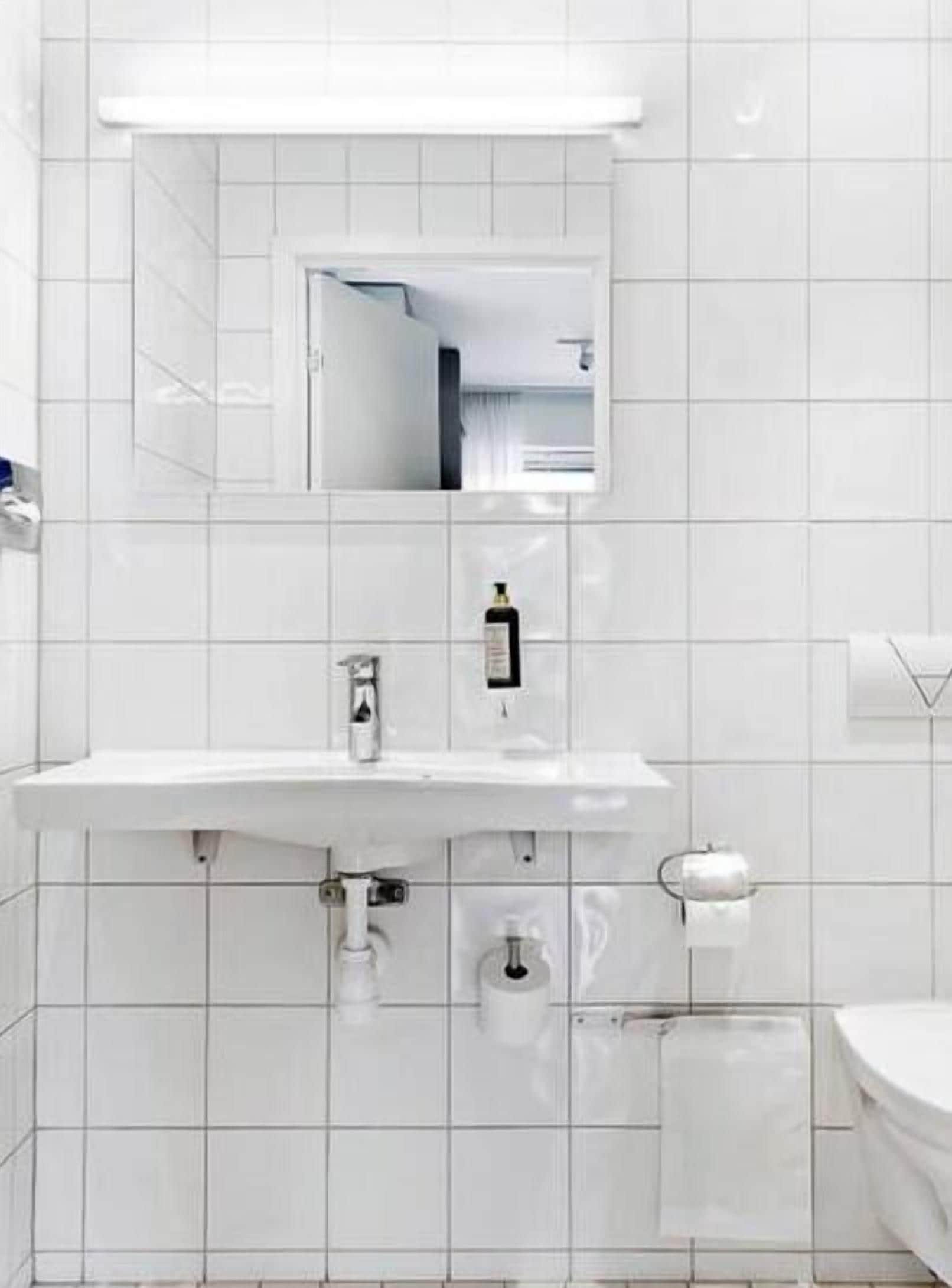 Un baño moderno con azulejos blancos, un lavamanos con espejo, un perchero y un inodoro.