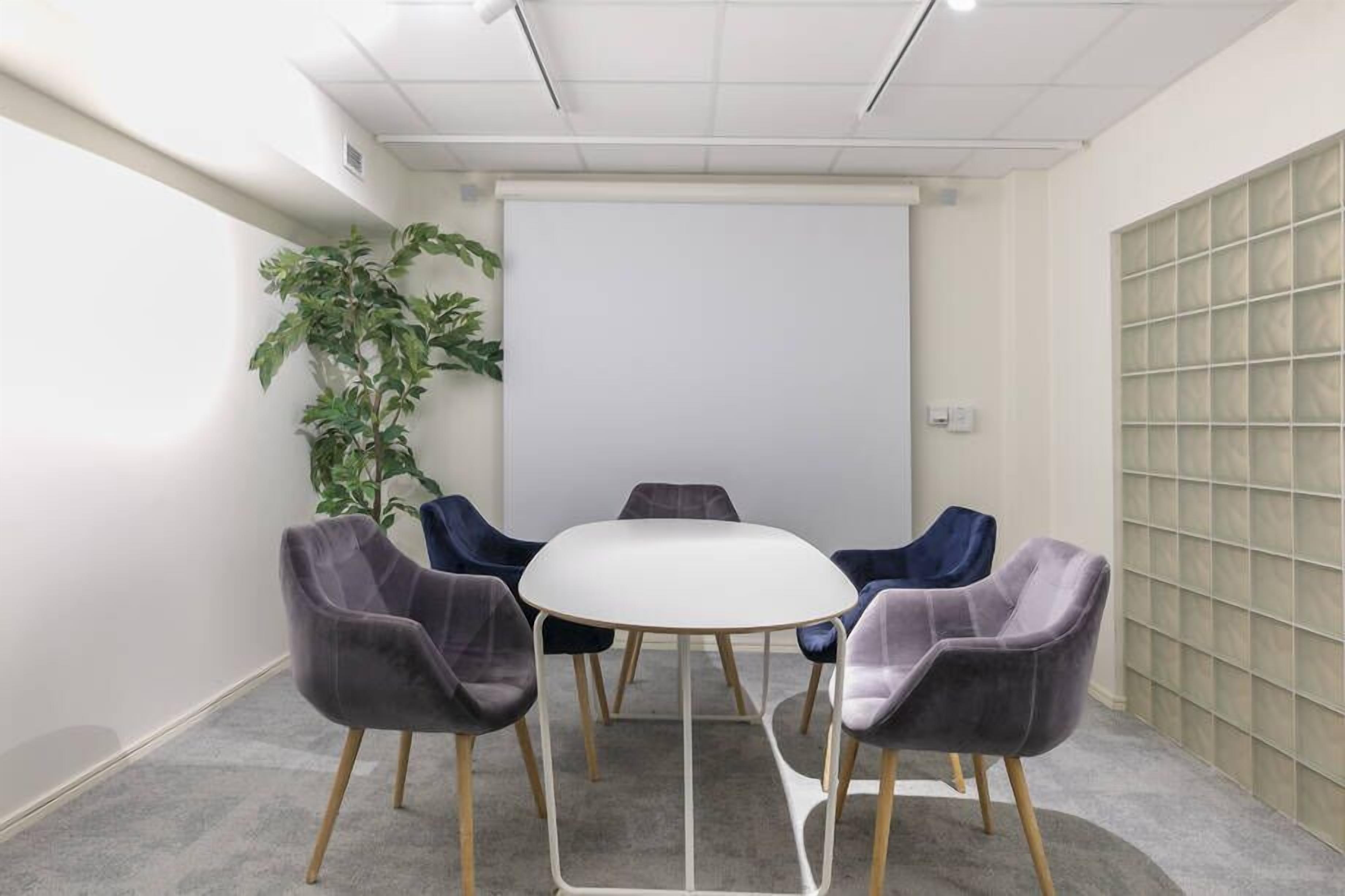 Une salle de conférence avec une table blanche entourée de quatre chaises, une plante en pot et un tableau blanc.
