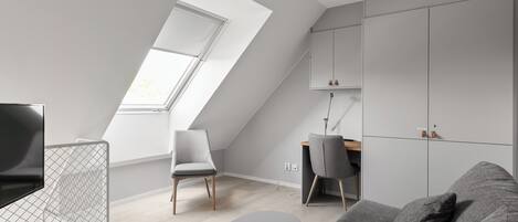 A modern loft apartment with a sloped ceiling, a dining area, a gray sofa, and a TV.