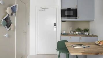 A compact kitchen with white cabinets, a microwave, and a sink. There's a dining table with a chair and a plate of fruit.