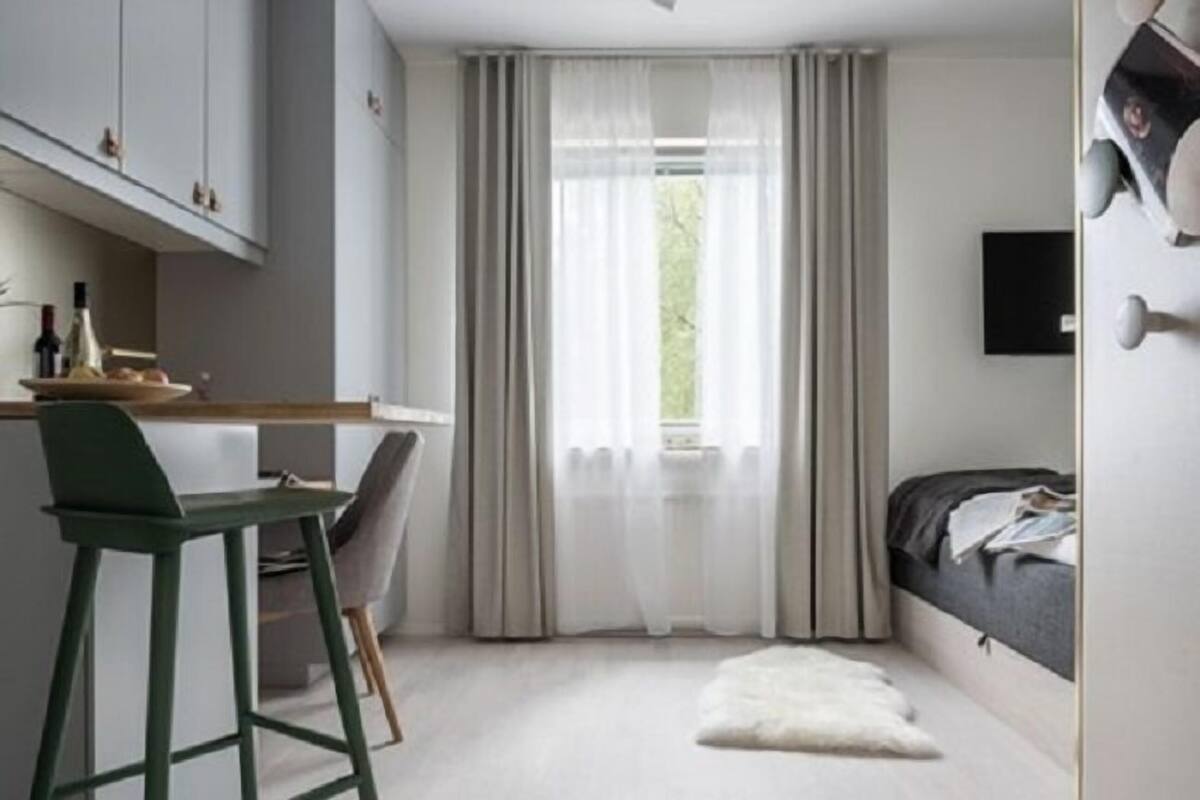 A bedroom with a bed, a desk, and a chair, a window with curtains, and a small rug.