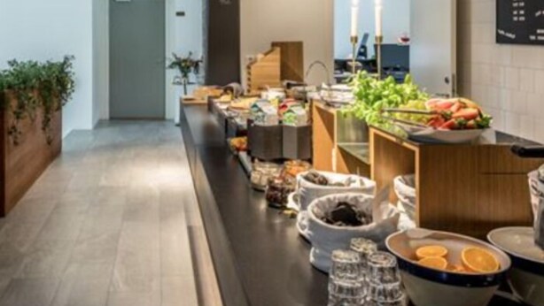 A modern hotel corridor with a long counter displaying various food items and beverages. - Avanti Hotel (Hägersten)