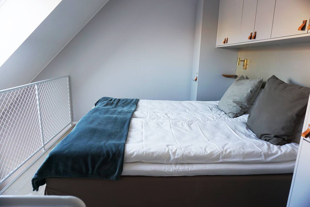 A bedroom with a bed, a blue blanket, and grey pillows.