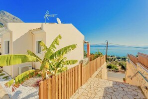 A building with a satellite dish, a wooden fence, and a stone pathway leading to a view of the sea.