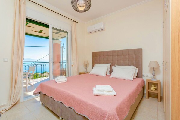 Quarto com cama, mesa de cabeceira, luminária, janela com vista e aparelho de ar condicionado.
