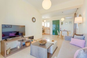 A modern living room with a flat-screen TV, a coffee table, a sofa, and a dining area with a table and chairs.