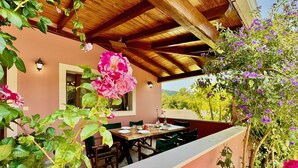 An outdoor dining area with a wooden table and chairs, surrounded by lush greenery and flowering plants. - Villa Cocoon Sidari with private pool (Sidari)