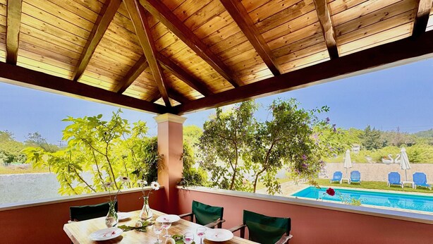 A wooden dining table with chairs, a vase with flowers, and empty plates. - Villa Cocoon Sidari with private pool (Sidari)