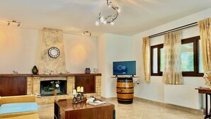 A living room with a fireplace, a television, and a wooden barrel. - Villa Cocoon Sidari with private pool (Sidari)