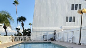 Vista de la piscina con una tumbona, la piscina y un edificio blanco al fondo.
