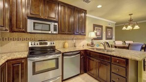 Una cocina con gabinetes de madera, electrodomésticos de acero inoxidable, encimera de granito y un comedor con candelabro.