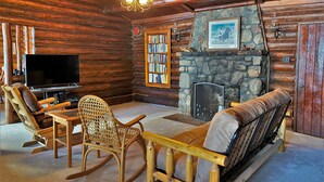 A log cabin interior with a stone fireplace, wooden furniture, a television, and a bookshelf. - Lakeside Lodge on Lake Huron (Saint Ignace)