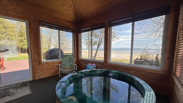 A wooden cabin with a glass hot tub, large windows, and a view of the beach. - Lakeside Lodge on Lake Huron (Saint Ignace)