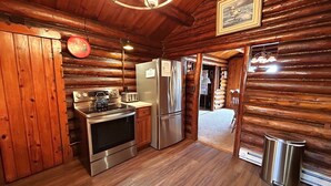 A log cabin interior with a kitchen featuring a stove, oven, refrigerator, and a dining table. - Lakeside Lodge on Lake Huron (Saint Ignace)