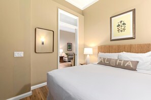 Quarto de hotel com uma cama, mesa de cabeceira, abajur, quadro emoldurado e porta que dá para outro cômodo.