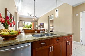 A kitchen with granite countertops, stainless steel appliances, wooden cabinets, and a bowl of fruit. - Honua Kai | Mountain View 2 BR | Free Car w/ 6+ Nights | HKK-112 (Lahaina)