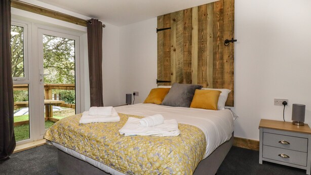 Camera da letto con un ampio letto, una testiera in legno, un comodino e vista sull'esterno.