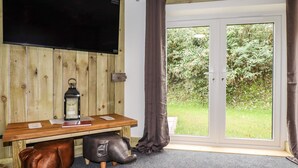 Una stanza con parete in legno, televisione a schermo piatto, un tavolo con una lanterna e vista sul verde attraverso una porta vetrata.
