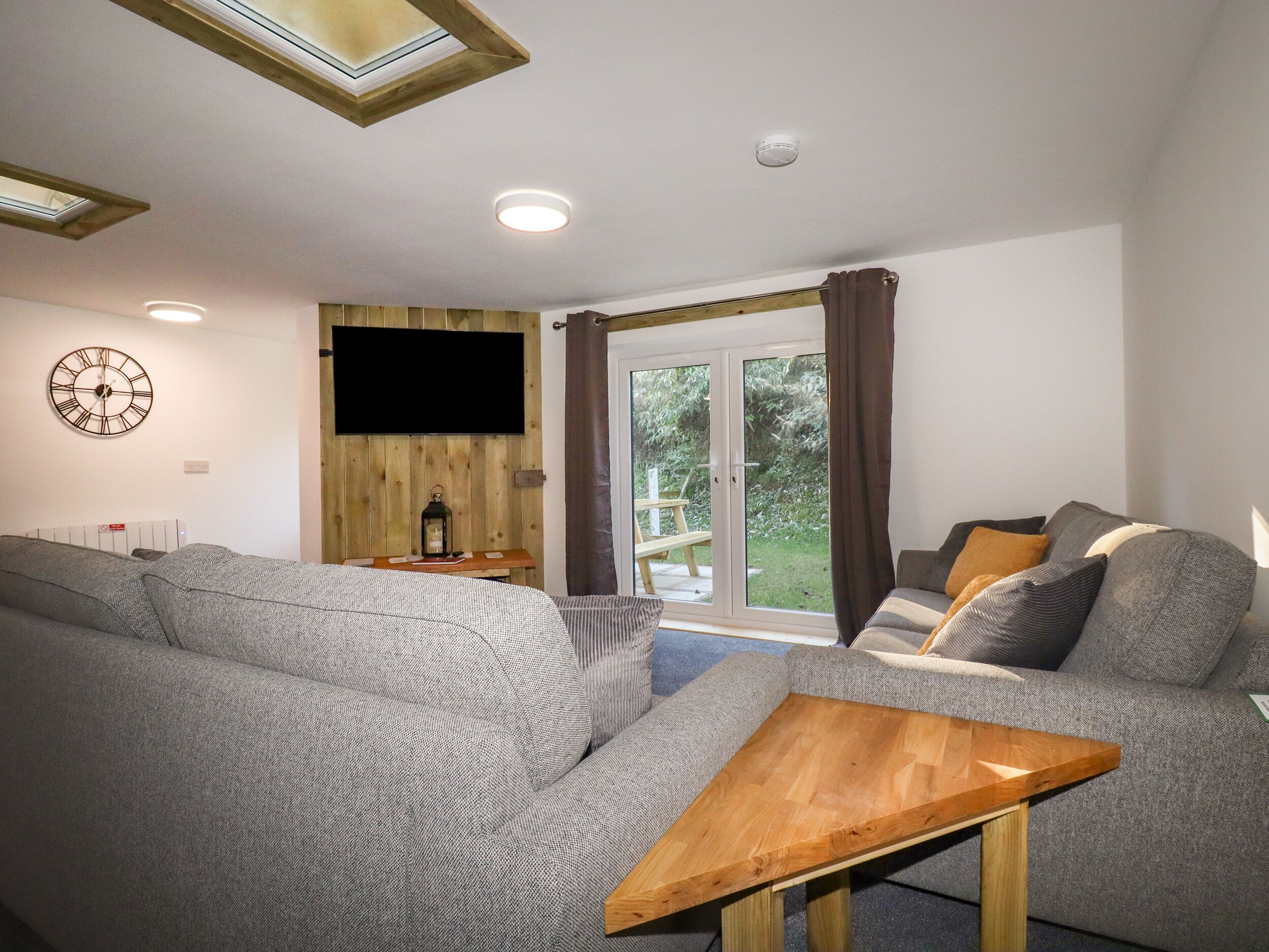 A modern living room with a grey sofa, a wooden coffee table, and a television mounted on a wooden wall.