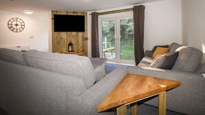 Un soggiorno moderno con un divano grigio, un tavolino in legno e una televisione fissata a una parete di legno.