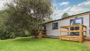 A building with a brick exterior, a wooden deck, and a large tree in the yard. - Stall 2 - The Stables (Truro)
