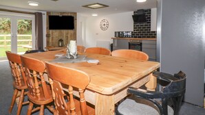 A dining area with a wooden table and chairs, a kitchen with a black backsplash, and a clock on the wall. - Stall 2 - The Stables (Truro)