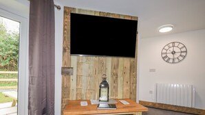 A room with a wooden wall panel, a mounted clock, a table with a lantern, and two elephant-shaped stools. - Stall 2 - The Stables (Truro)