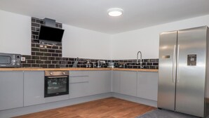 A modern kitchen with grey cabinets, a stainless steel refrigerator, a microwave, and a built-in oven. - Stall 2 - The Stables (Truro)