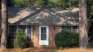 A single-story house with a brick exterior, a front door, and a small front yard with a pathway leading to the door. - Camden Cottage (Camden)