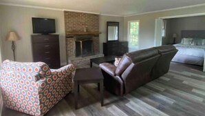 A living room with a fireplace, leather sofa, patterned armchair, and a television. - Camden Cottage (Camden)