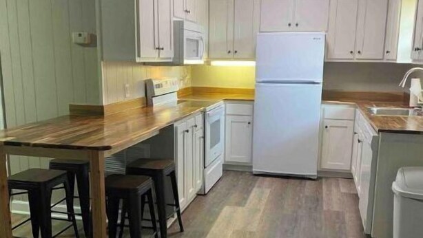 A compact kitchen with white cabinets, a wooden countertop, a built-in microwave, and a refrigerator. - Camden Cottage (Camden)