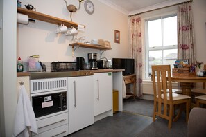 A compact kitchen with a microwave, oven, and coffee maker. There is a wooden table with chairs and a television. - Milton House-  Studio Apartment .Whitfield Suite (Leyburn)