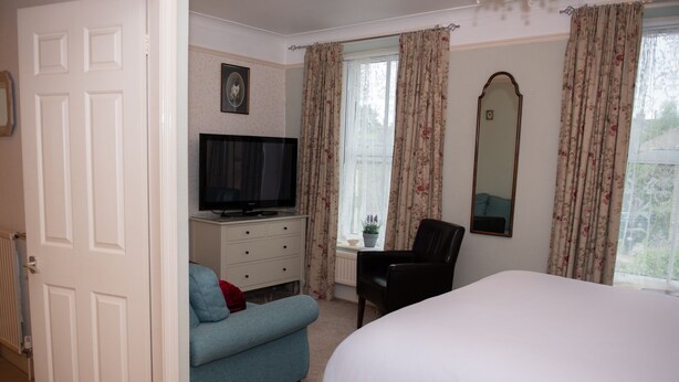A bedroom with a bed, a desk, a chair, a television, and a door.