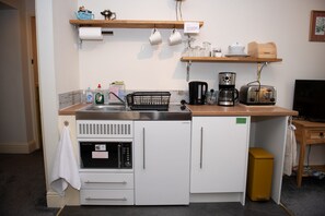 A compact kitchenette with a refrigerator, microwave, sink, and a coffee maker.