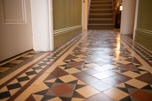 A hallway with patterned tile flooring and a staircase in the background.