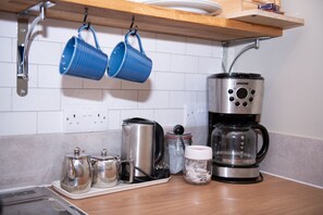 A kitchen counter with a coffee maker, two mugs, a kettle, and a jar of sugar.