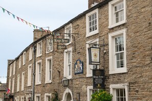Een historisch gebouw met meerdere borden waarop staat dat het het Kings Arms Hotel is, met een traditionele stenen gevel, meerdere ramen en een opvallend bord voor The Thesston Ales.