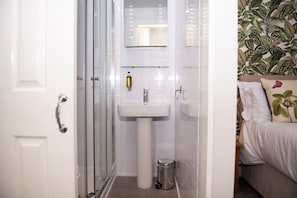 Un baño con cabina de ducha de vidrio, un lavamanos pedestal blanco y un pequeño cubo de basura.