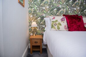 Ein Schlafzimmer mit einem Bett, einem Nachttisch, einer Lampe und einer Wand mit tropischem Blattmuster.