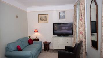 A hotel room with a bed, a sofa, a TV, a small table with a lamp, and a chair.