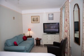 Een hotelkamer met een bed, een bank, een televisie, een klein tafeltje met een lamp en een stoel.