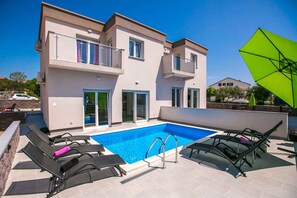 Un bâtiment à deux étages doté d’une piscine, d’un espace extérieur aménagé et d’un parasol vert.