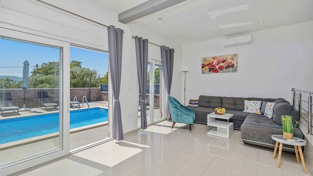 Un salon moderne avec vue sur la piscine, un canapé gris et une petite table d’appoint.